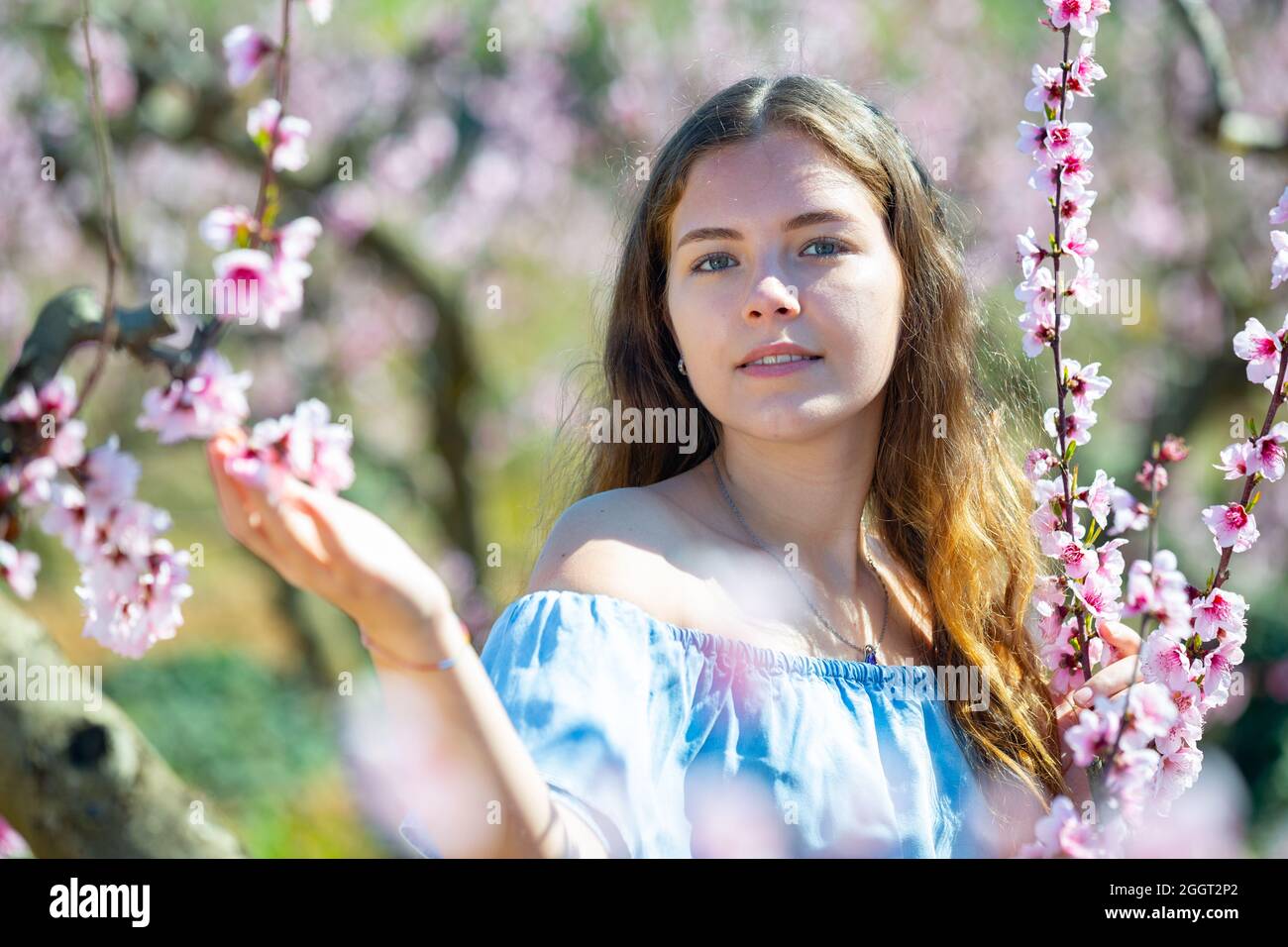 Portrait of young smiling woman in a garden with blooming peach trees Stock Photo