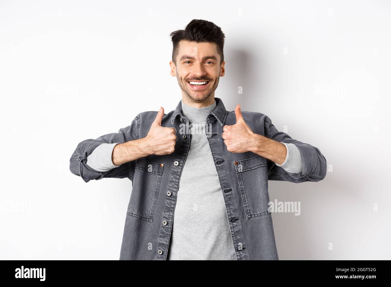 Handsome smiling man showing thumbs-up in approval, praise good 