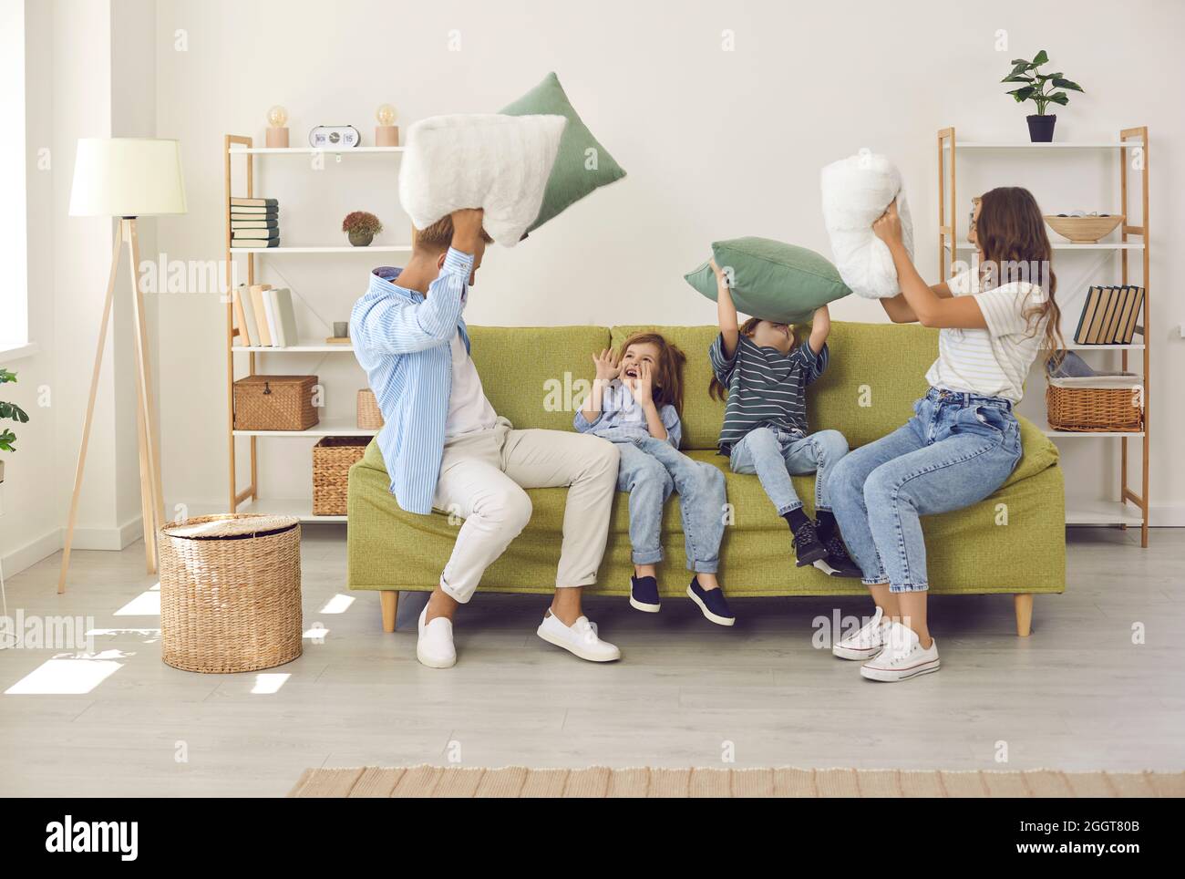 Happy young mother, father and children having a pillow fight on sofa in living room Stock Photo