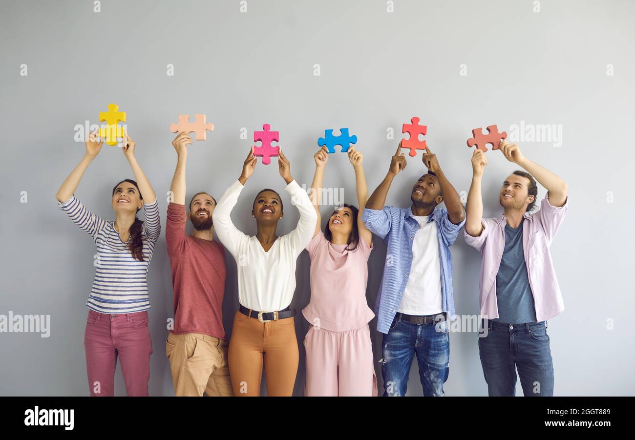 Group of happy smiling multiracial young people holding colorful puzzle pieces over their heads. Stock Photo