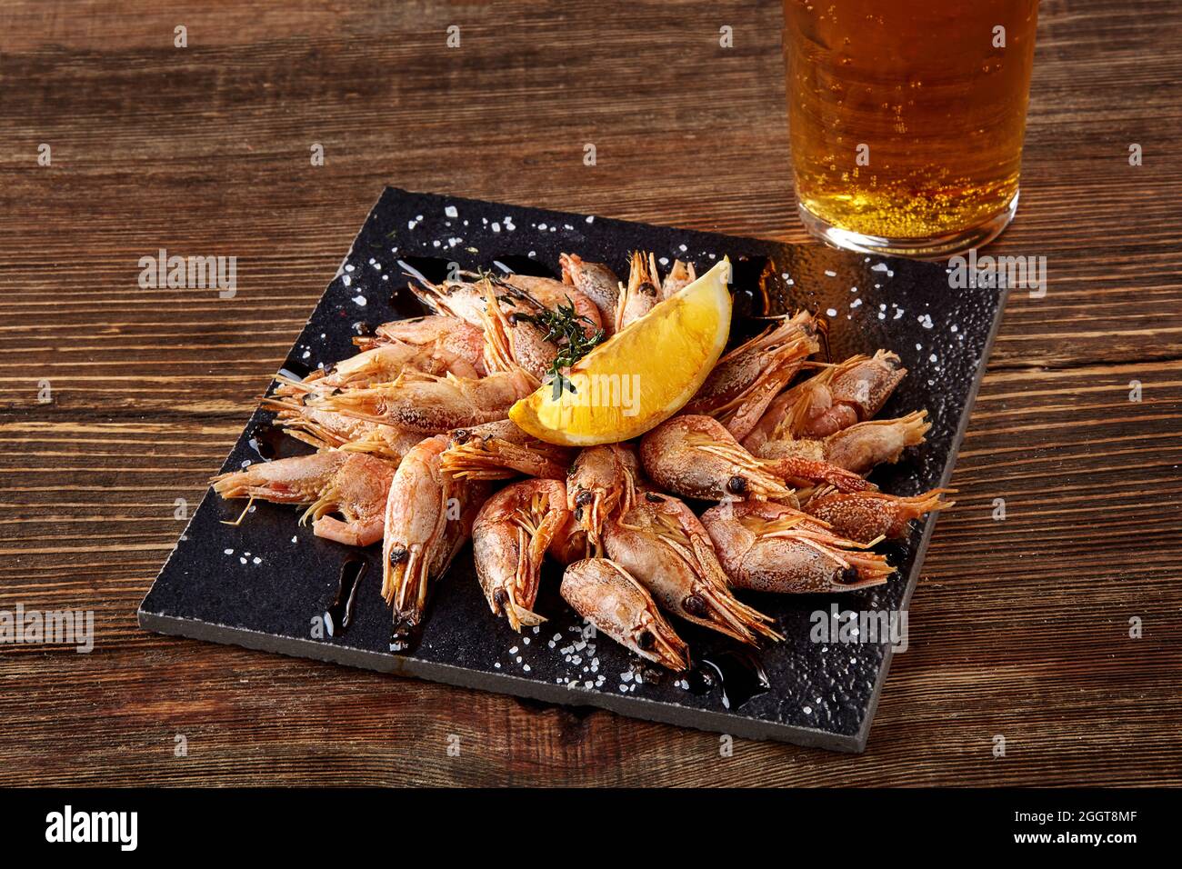Grilled shrimps on black board pan and beer on wooden table Stock Photo