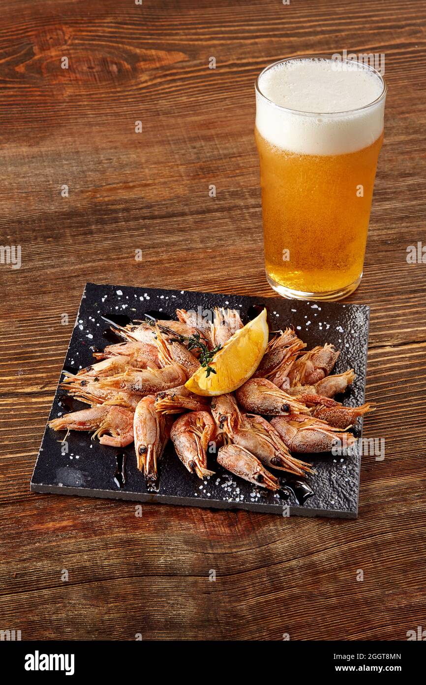 Grilled shrimps on black board pan and beer on wooden table Stock Photo