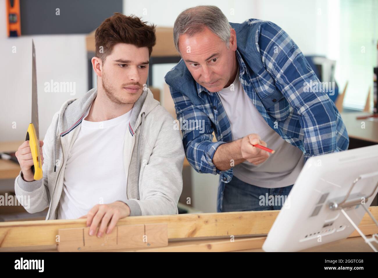 senior and craftsman apprentice together at laptop computer in workshop ...