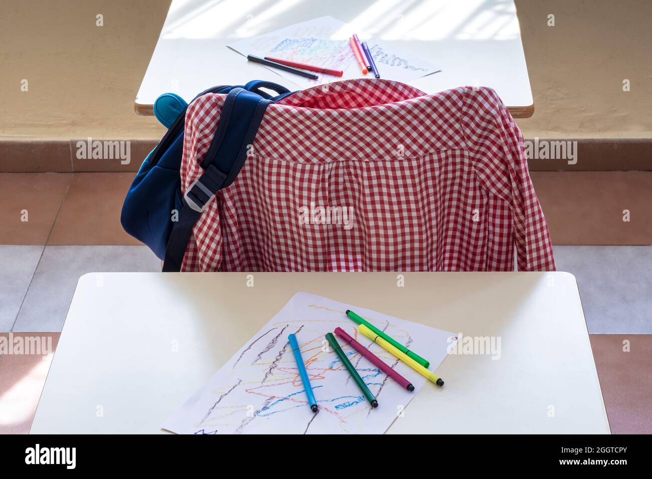 Photograph of the classroom of a primary school.In the photo you can see a school apron hanging on a chair, some drawings and some colored markers.The Stock Photo
