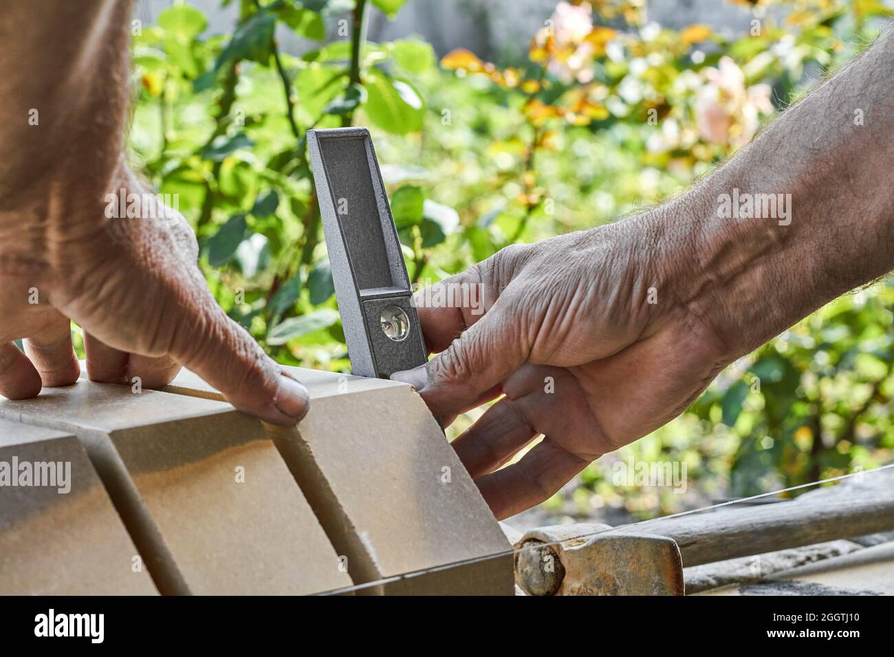 Bricklayer levelling bricks on the new fence from facing bricks using building level. Stock Photo