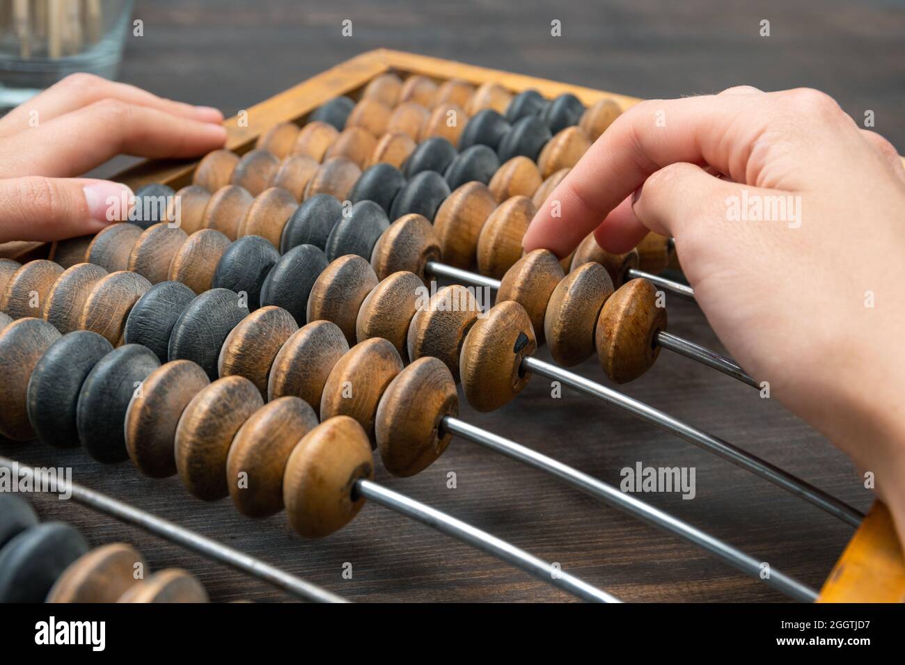 Female hand counting on ancient retro old abacus, moving beads on a wooden background, copy of space, close-up. Business and financial concept. Saving Stock Photo