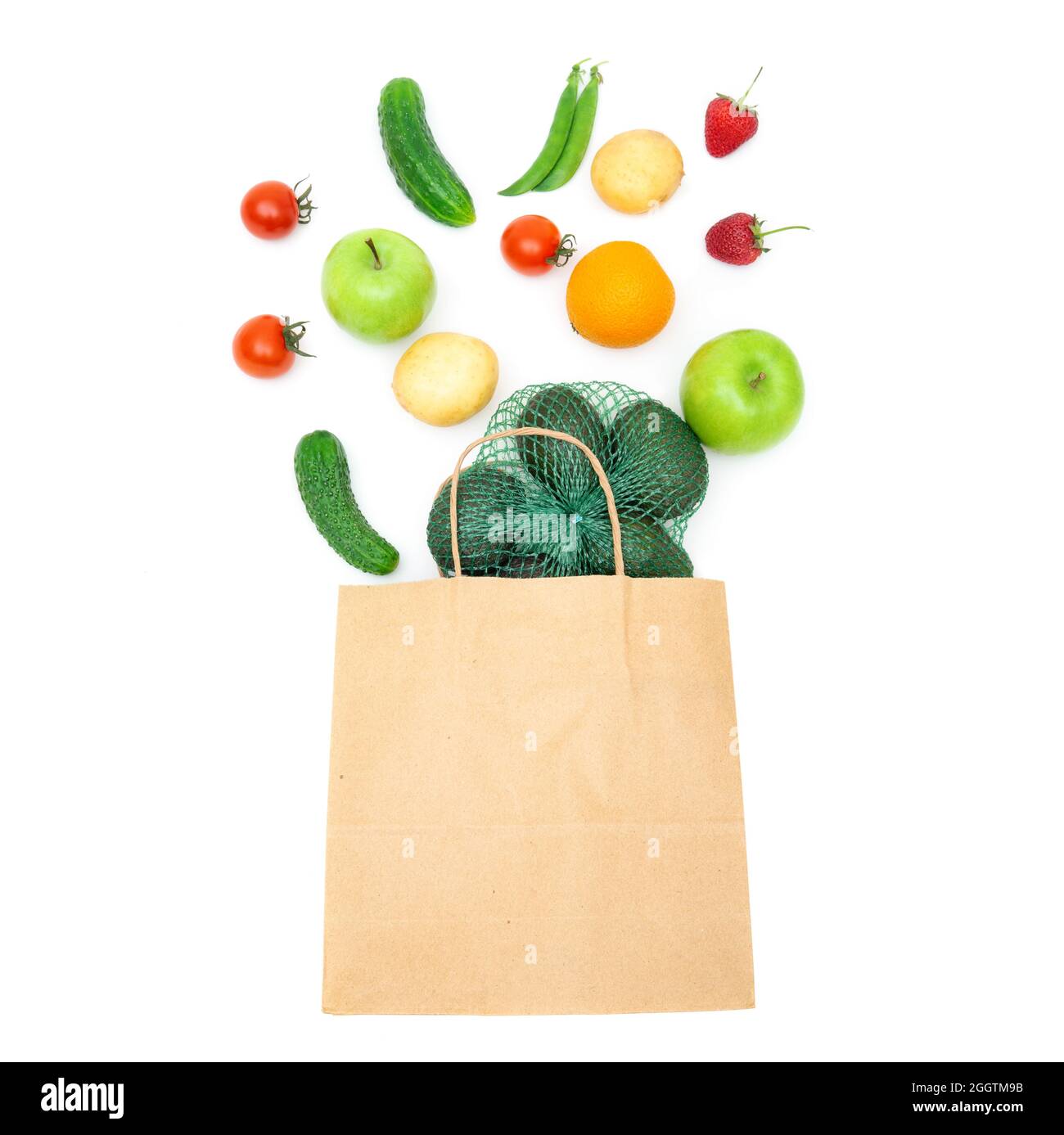 Assorted fruits and vegetables falling into a craft paper shopping bag isolated on white. Creative organic groceries flat lay. Stock Photo