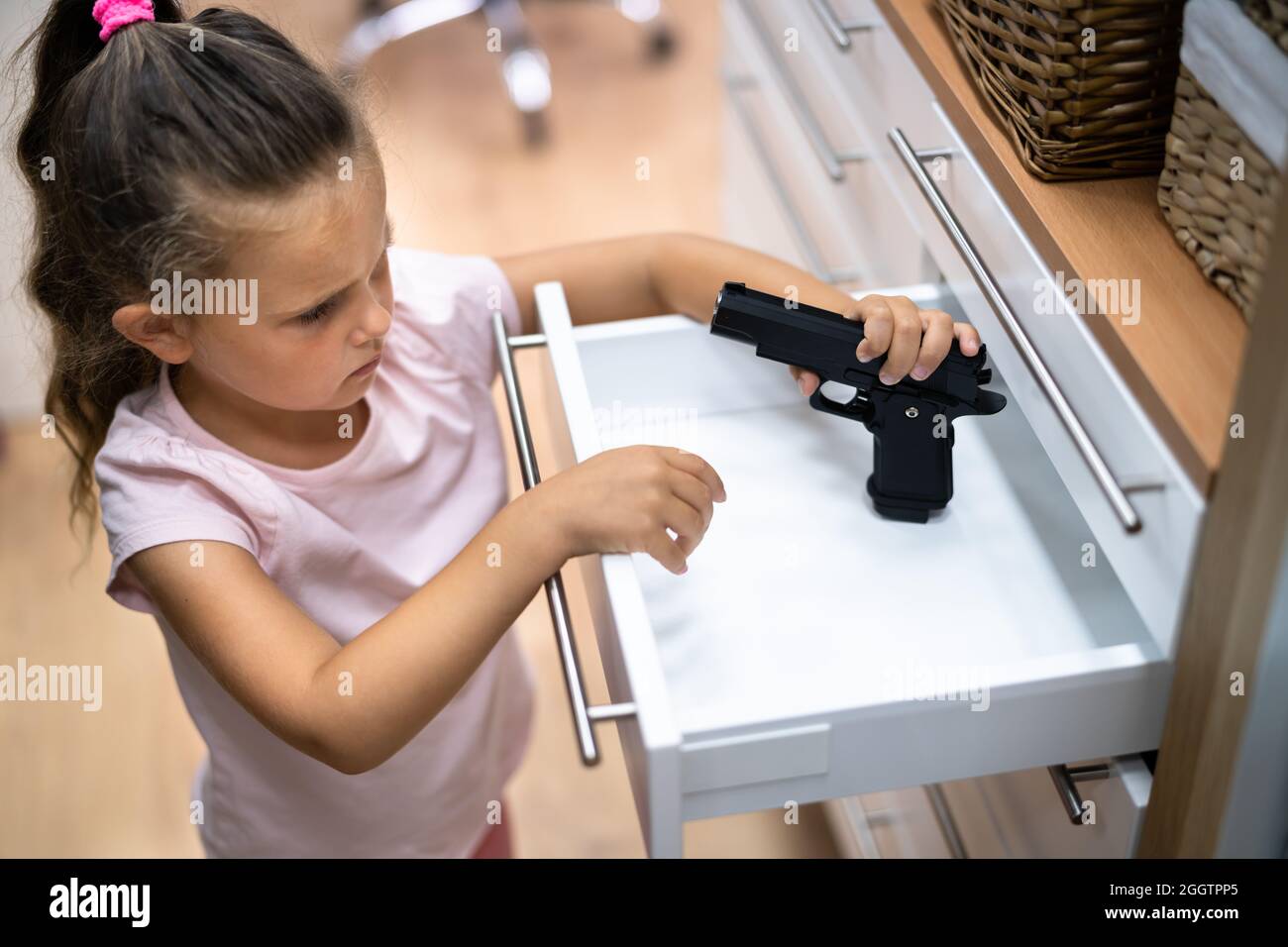 Kid With Gun. Girl Reaching For Pistol In Drawer. Children Safety Stock Photo