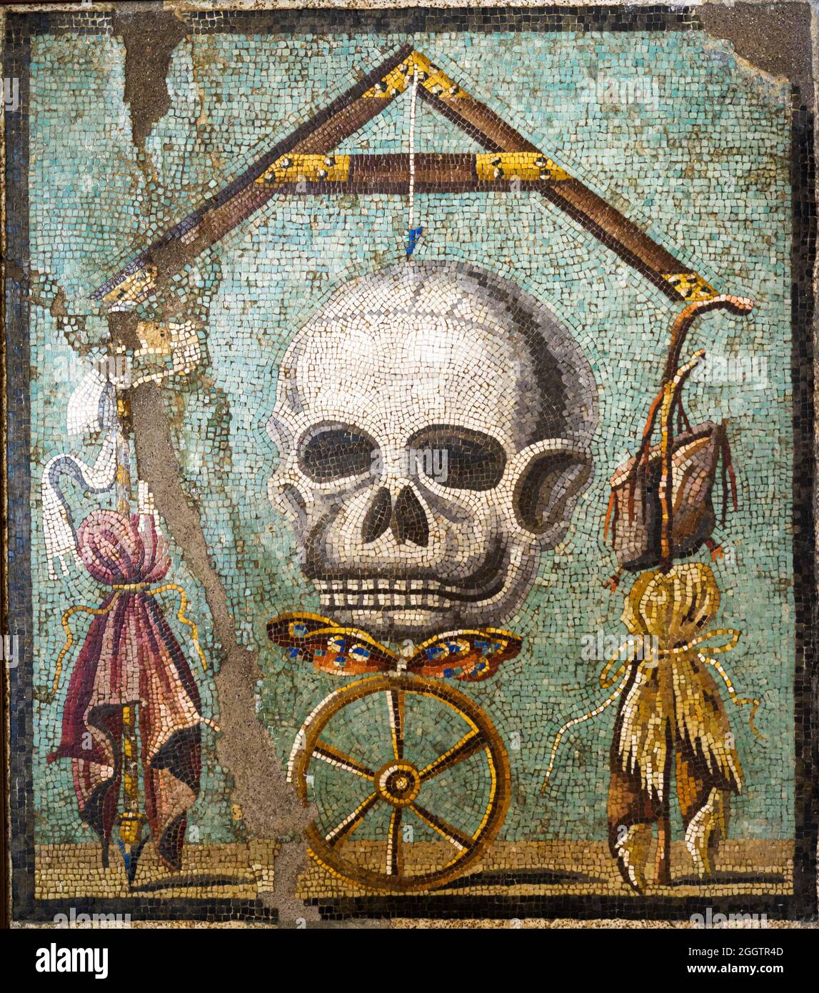 Memento Mori Mosaic emblema in opus vermiculatum made from polychrome tesserae. The mosaic depicts the allegory of death which levels distinctions between human beings. At the top of the composition there is a plumb-bob with its plumb-line whose axis is death in the form of a skull; below there is a butterfly, the soul, on a wheel, symbolising Fortune: between the arms of the plumb-blob are the symbols of poverty on the right (the saddlebag, the beggar's stick and the cloak) and the symbols of wealth on the left (the sceptre, purple and the crown).  Pompeii, casa bottega (shop house) - Italy Stock Photo