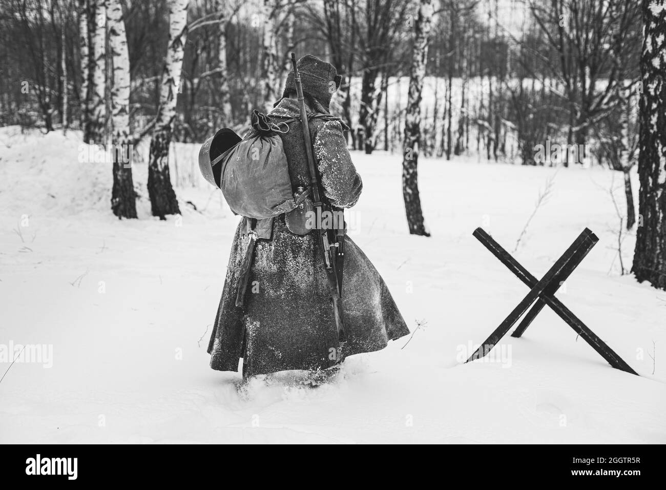 World War II Russian Soviet Red Army Soldier Marching Through Snowy Winter Forest Forest. Soldier Of WWII WW2 Times. Black And White Photo. Stock Photo