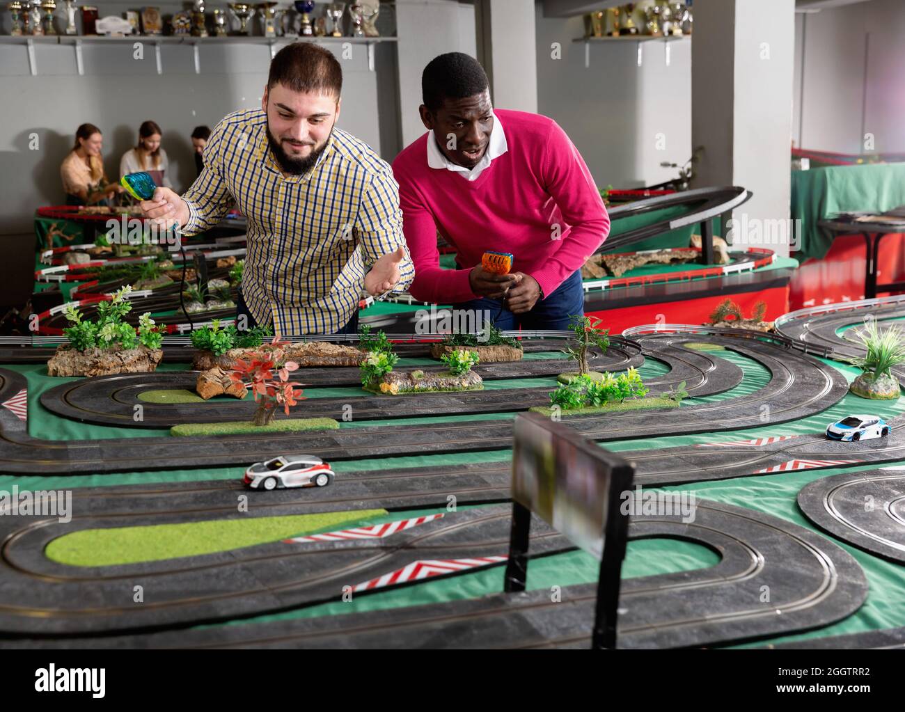 Two adult men playing with childrens slot car racing track Stock