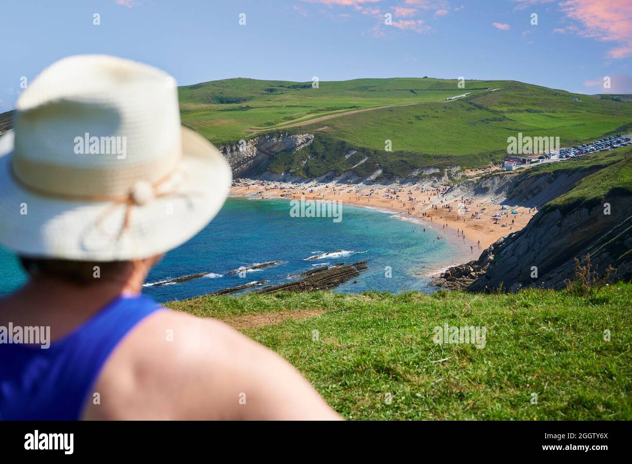 Blur of middle-aged woman with straw hat in foreground in front of Sable de Tagle beach,Suances, Cantabria, Spain, Europe Stock Photo