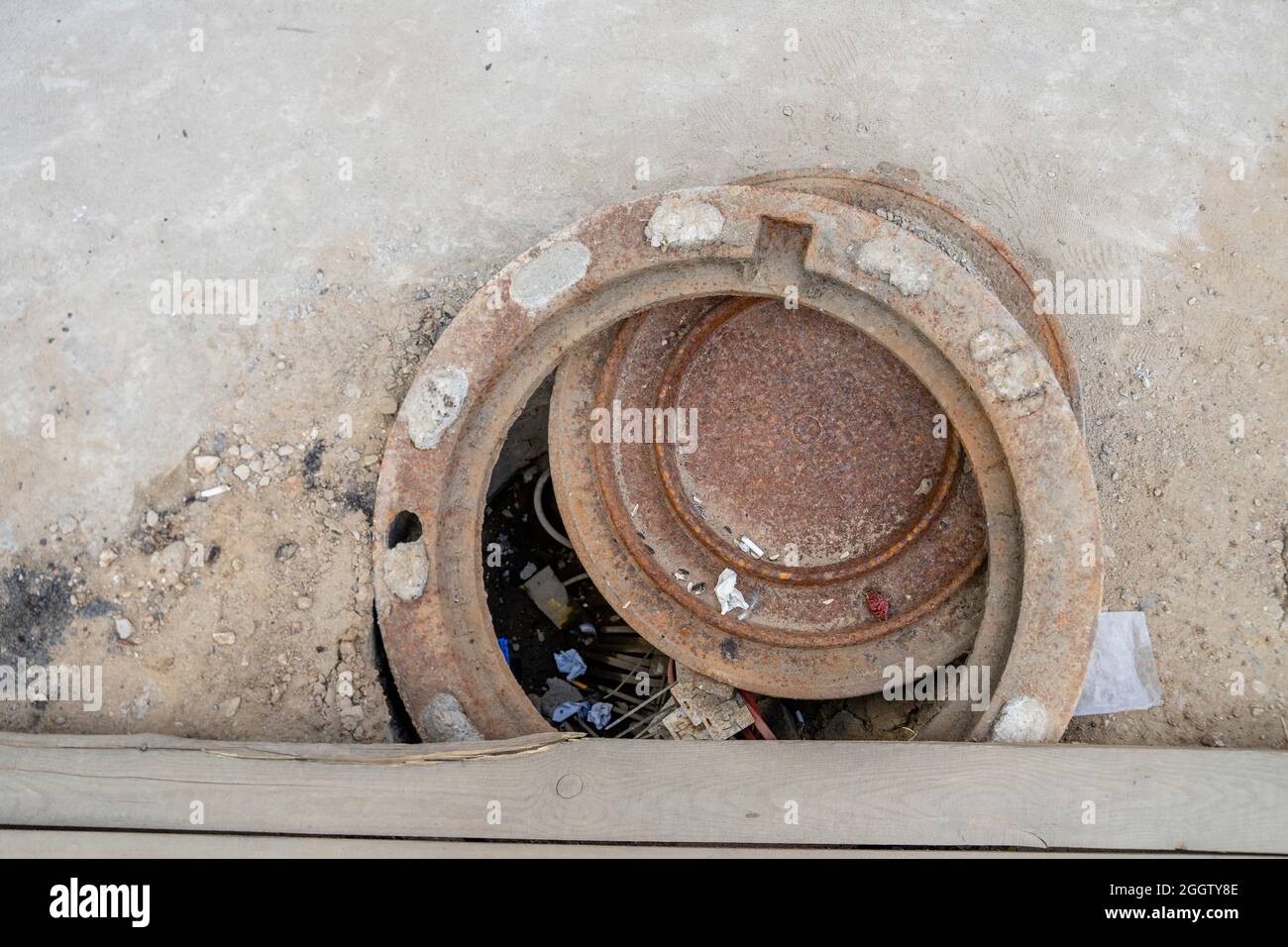 Misplaced rusty circular sewer lid over the drain hole with garbage inside, Moscow, Russia Stock Photo