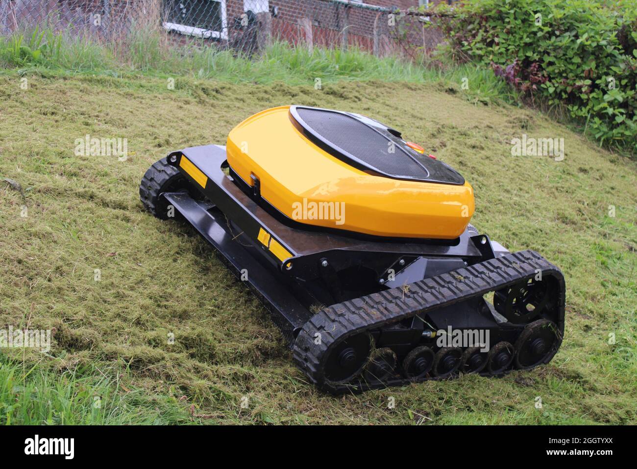 Remote controlled agricultural grass and bush cutter on a steep grassy bank. Robotic lawn mower. Stock Photo