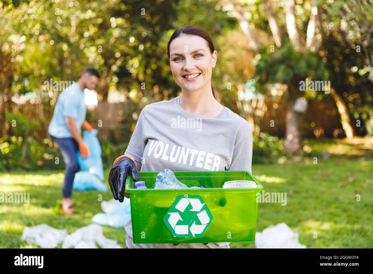 Portrait of smiling caucasian woman holding recycling box, cleaning up countryside with husband Stock Photo
