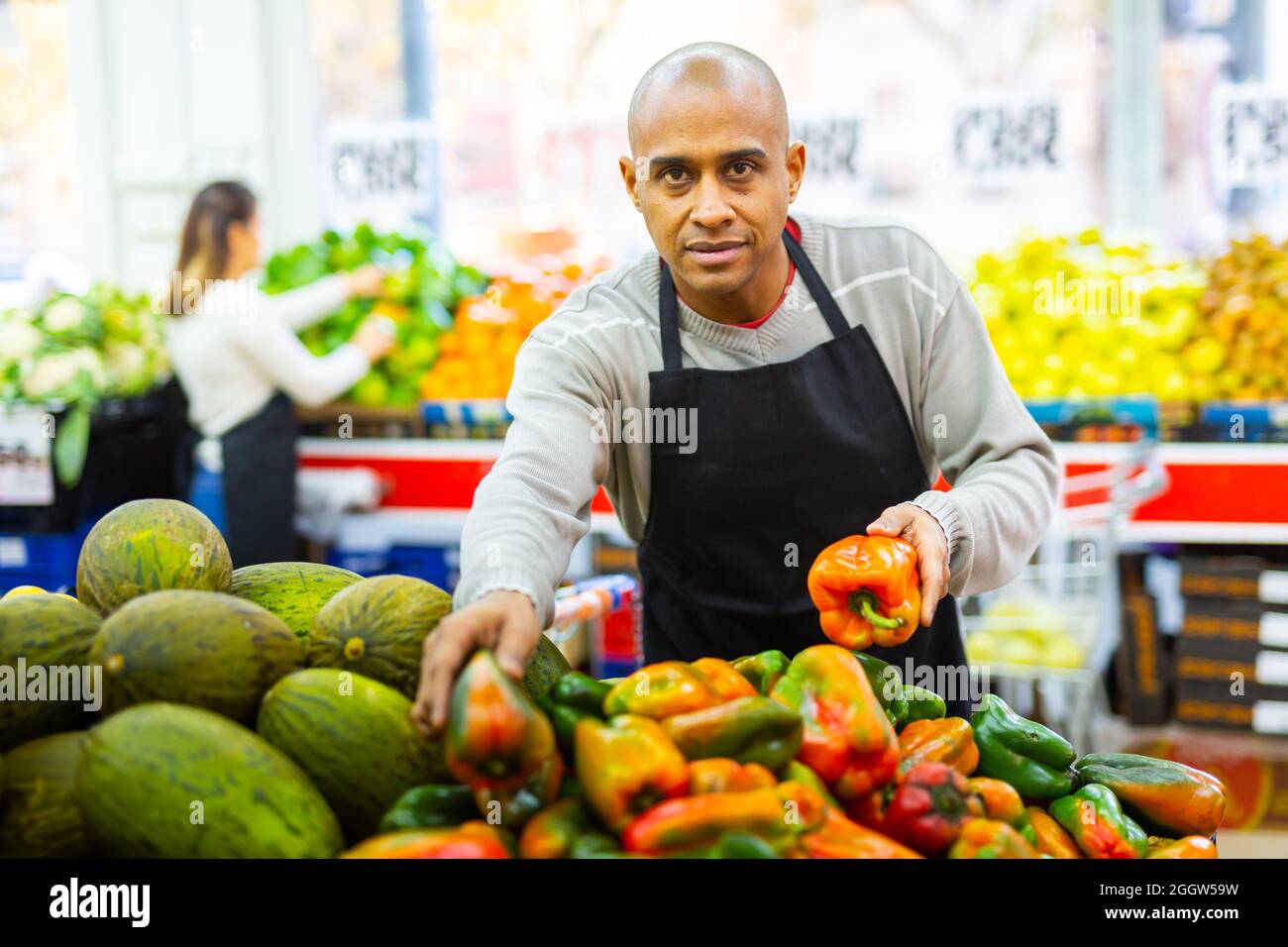 Merchandiser in an apron lays out ripe bell peppers on supermarket