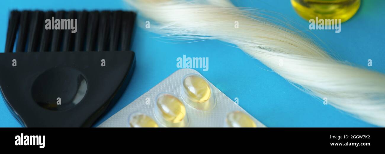 Vitamins and hair oil together with brush lie on dove background Stock Photo