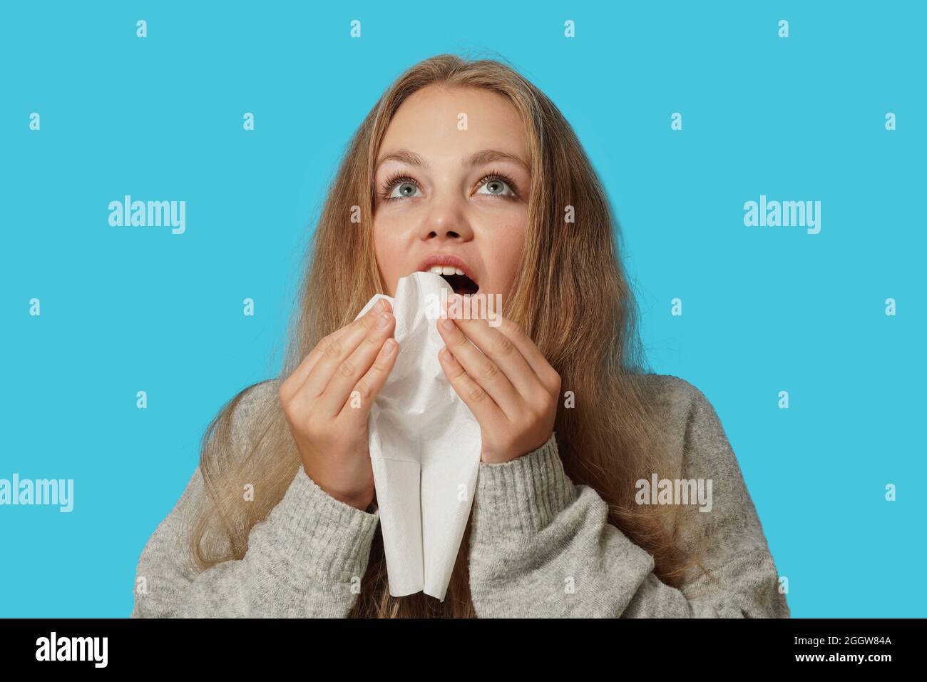 Young blond woman suffering from allergy on light blue background