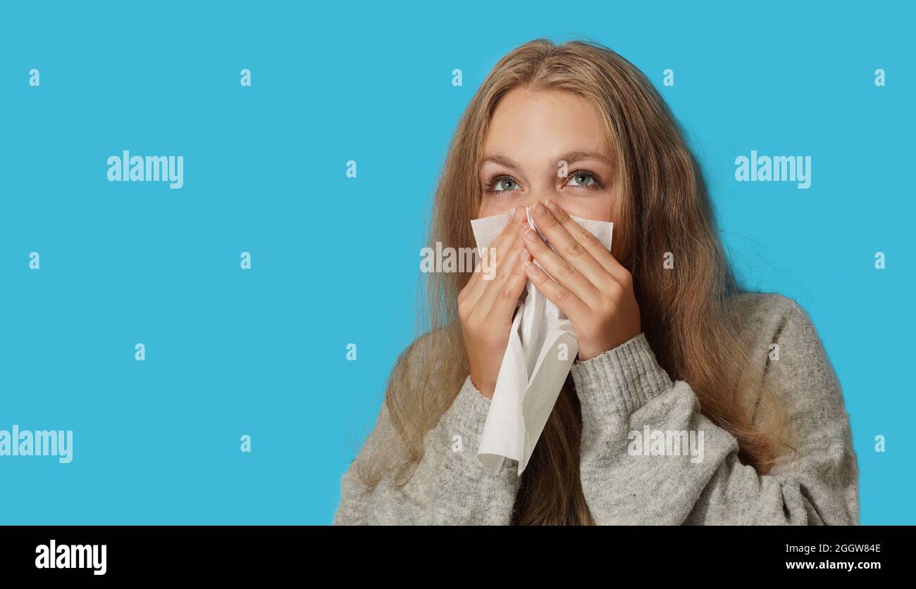 Young blond woman suffering from allergy on light blue background