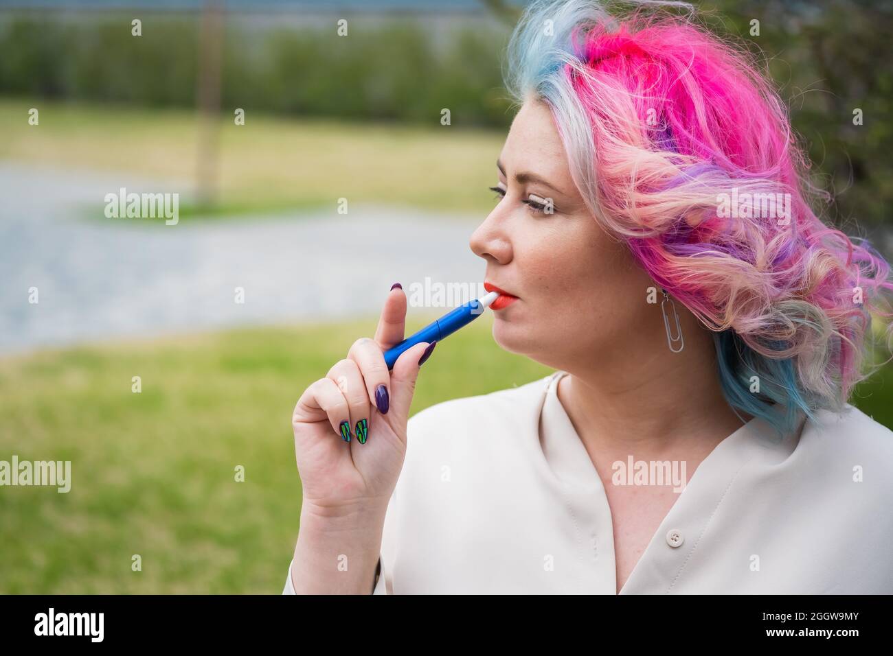 Caucasian woman with colored hair smokes an electronic cigarette. Stock Photo