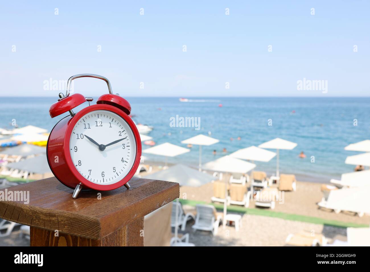 Red alarm clock standing on sea beach of hotel closeup Stock Photo