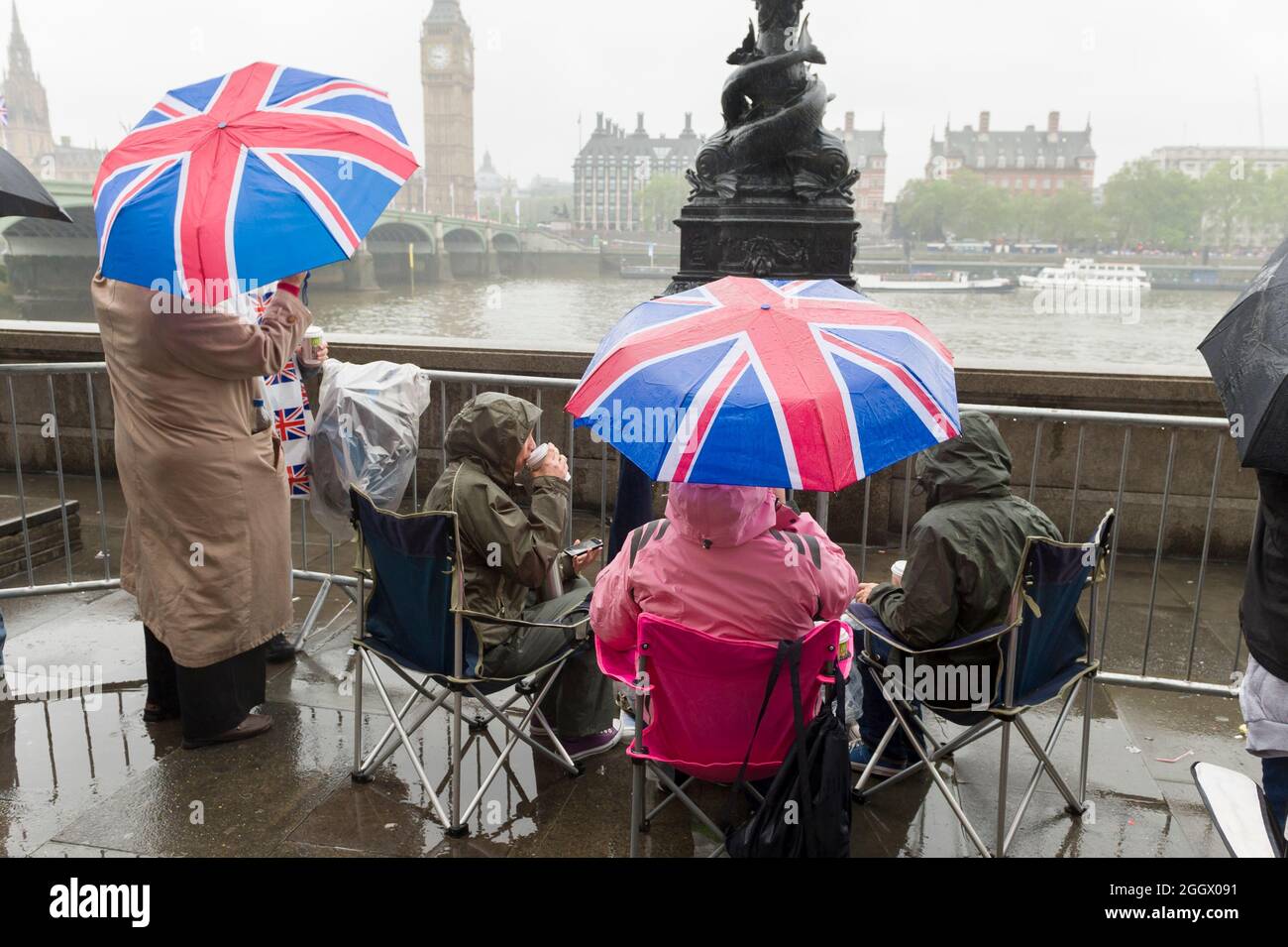 Spectators waiting under  Union Jack umbrellas in the rain for The Thames Diamond Jubilee Pageant to pass the South Bank, London. The Pageant was made up of hundreds of boats that sailed from Battersea Bridge to Tower Bridge to celebrate Queen Elizabeth II's 60 years on the throne. Millions of people lined the banks of the Thames to watch the spectacle.  South Bank, London, UK.  3 Jun 2012 Stock Photo