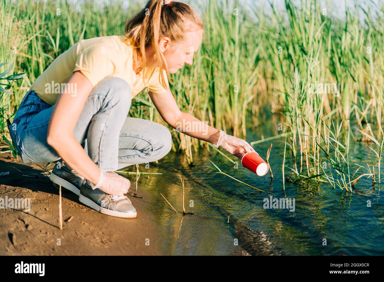 Young female volunteer satisfied with picking up trash, a plastic bottles  and coffee cups, clean up beach with a lake. Woman collecting garbage in  bag Stock Photo - Alamy