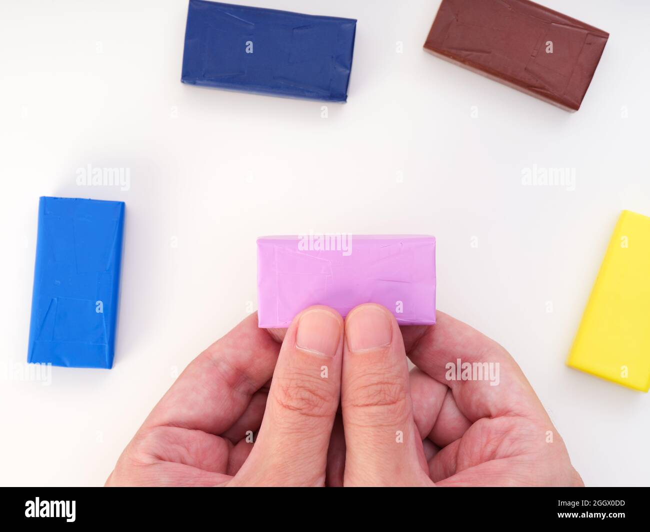 A man holding a pink piece of polymer clay in his hands with other pieces of polymer clay around them. Close up. Stock Photo