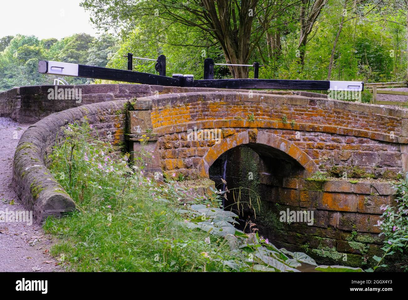 A beautiful stone bridge spanning the canal near Marple, Cheshire with imposing black and white painted lock gates . Stock Photo