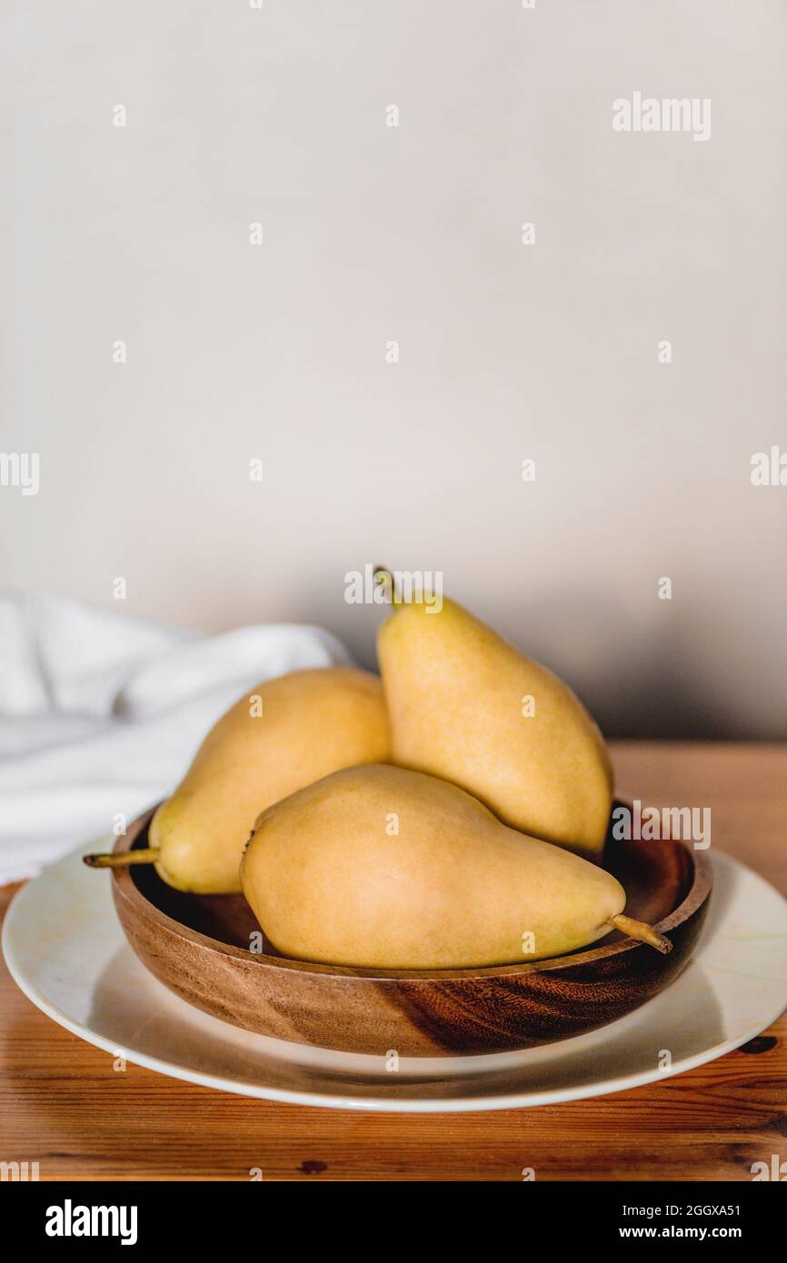 Three organic pears in wooden plate on wooden table. Stock Photo