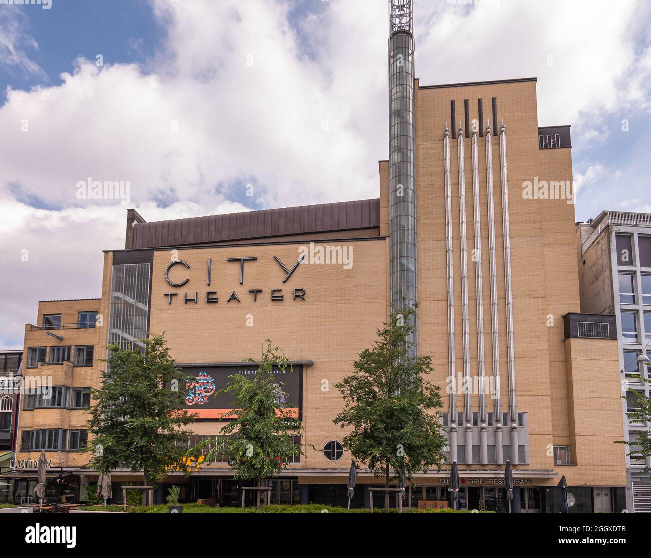 Amsterdam, Netherlands - August 15, 2021: large light brown City Theater building is cinema first under blue cloudscape with green trees in front. Stock Photo
