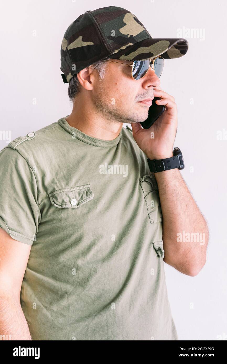 Military man with camouflage cap and sunglasses, talking on the phone ...