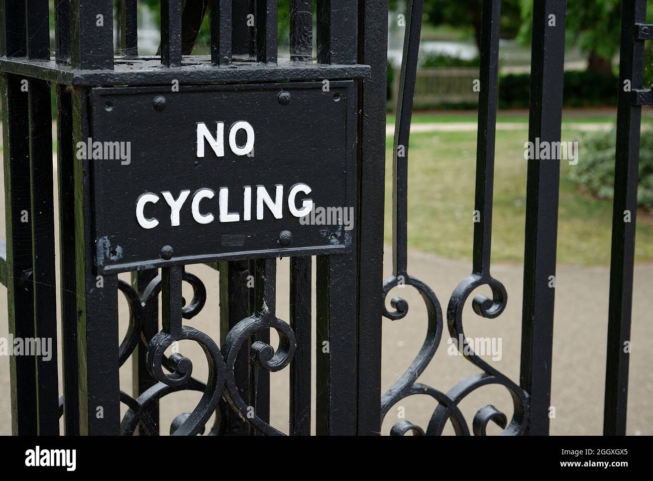 An old No Cycling sign at the entrance to a park in England, UK. A black painted metal sign on wrought iron gates. Stock Photo