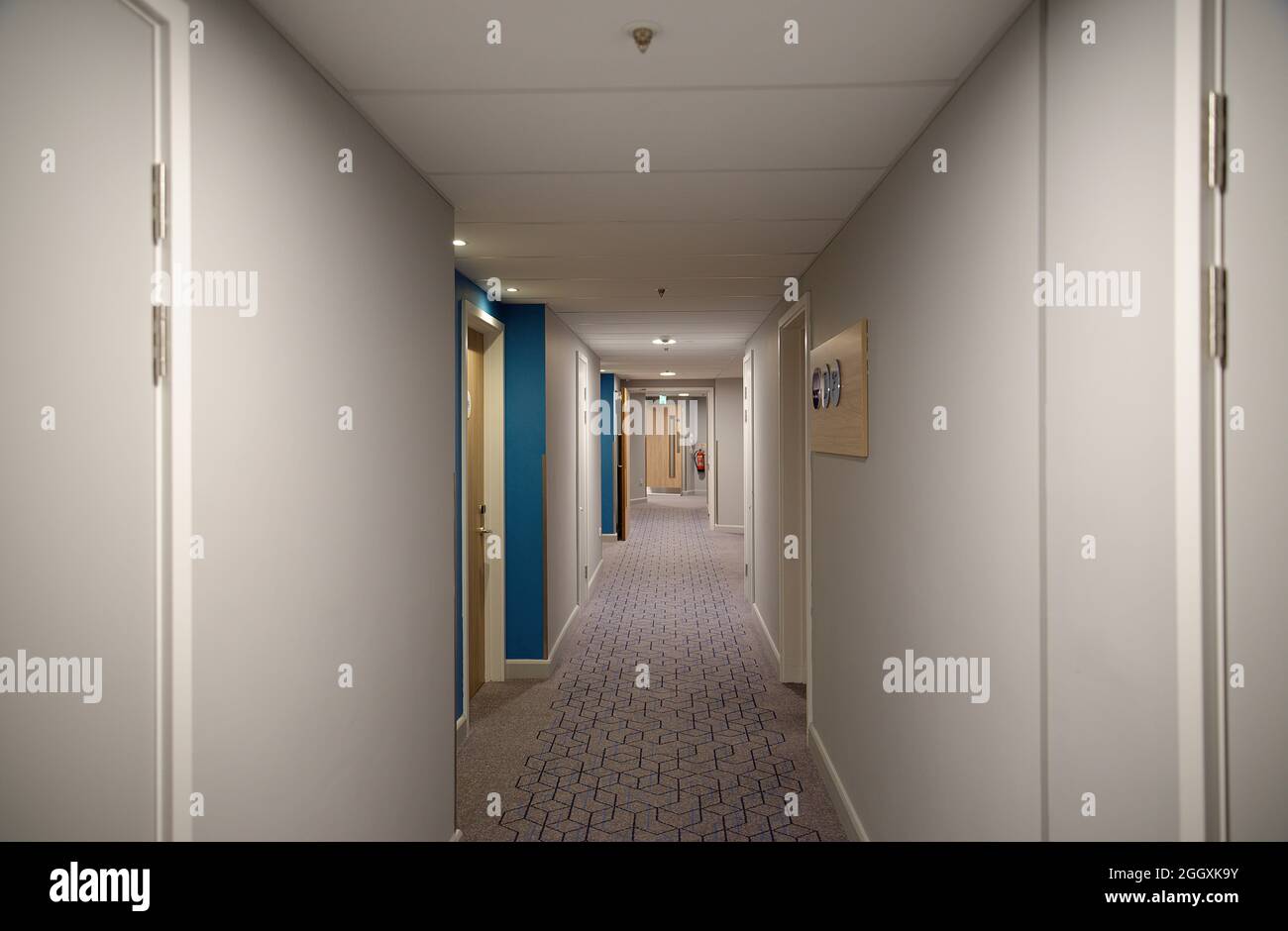 A dimly lit hotel corridor with plain walls and a patterned carpet. Stock Photo