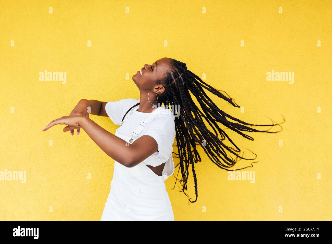 Side view of young happy woman with long braids dancing at yellow wall ...