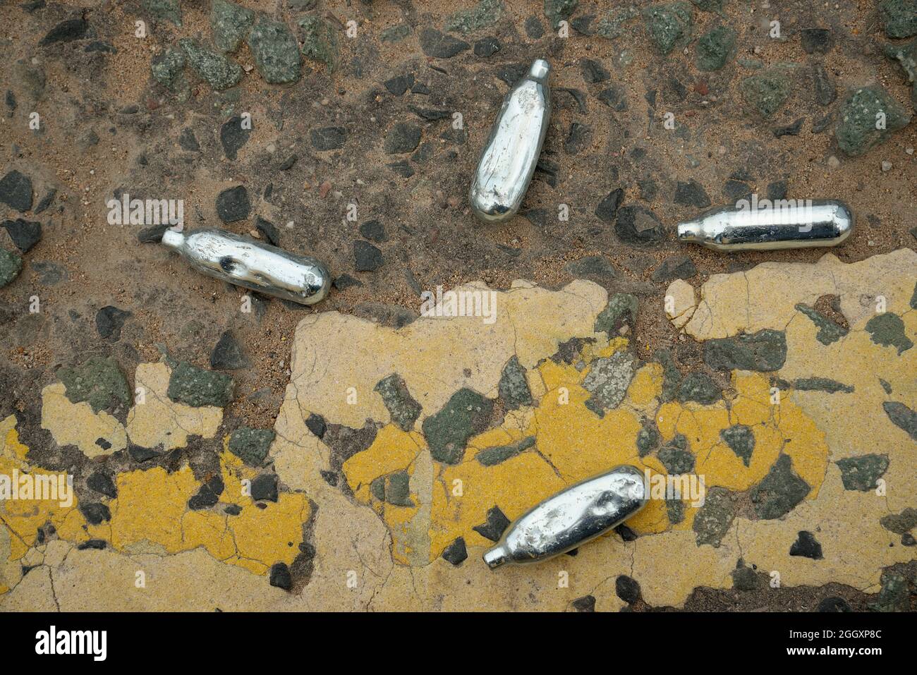 Nitrous Oxide gas canisters discarded on a street corner. Small silver gas cartridges used to fill balloons. Stock Photo