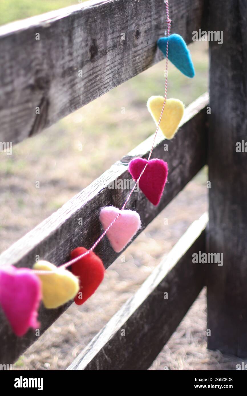 A rainbow colored garland made of hearts hanging from a wooden fence. Stock Photo