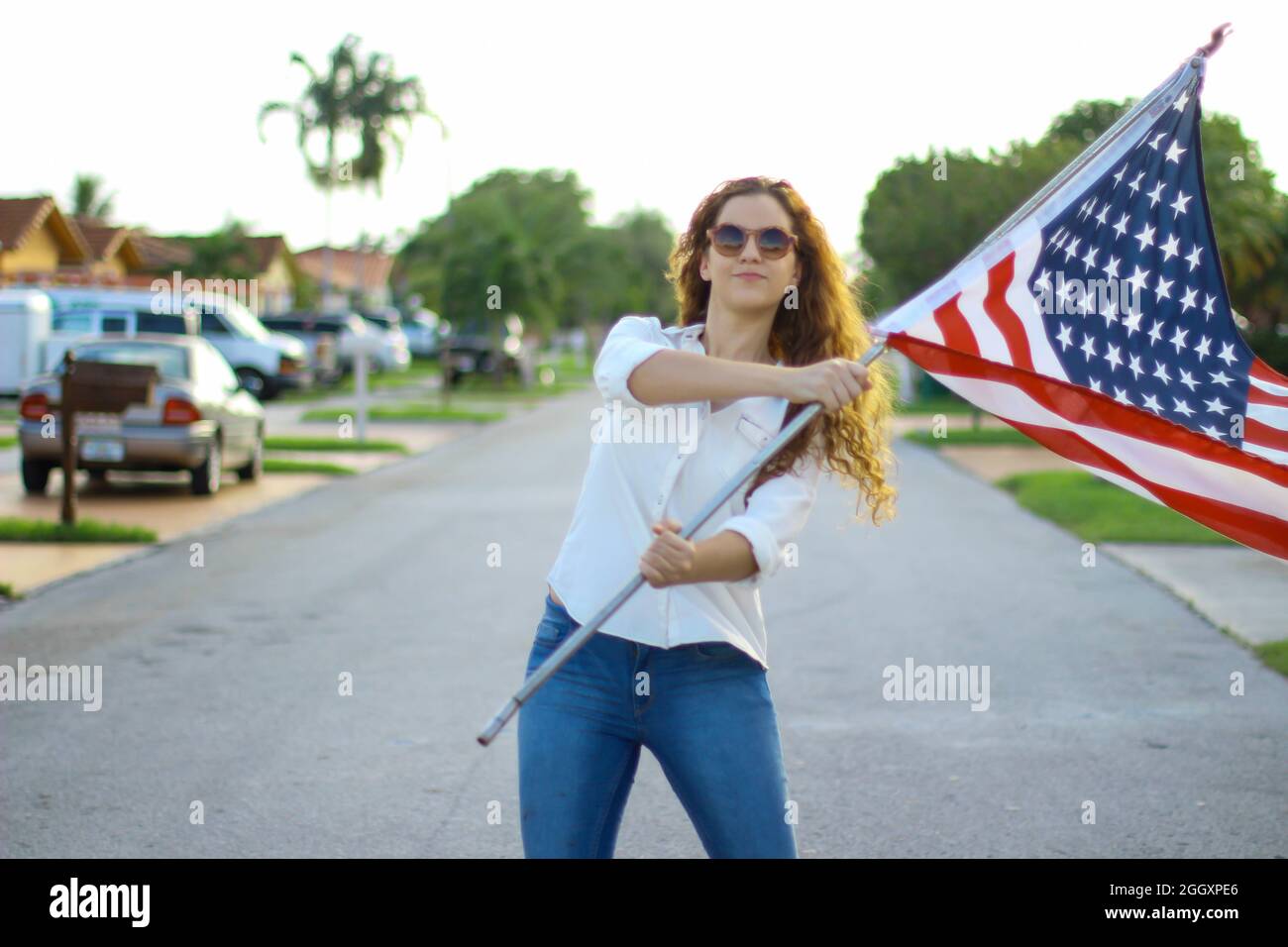 Young redhead Hispanic and Caucasian woman wearing sunglasses waving the American flag outside. Stock Photo