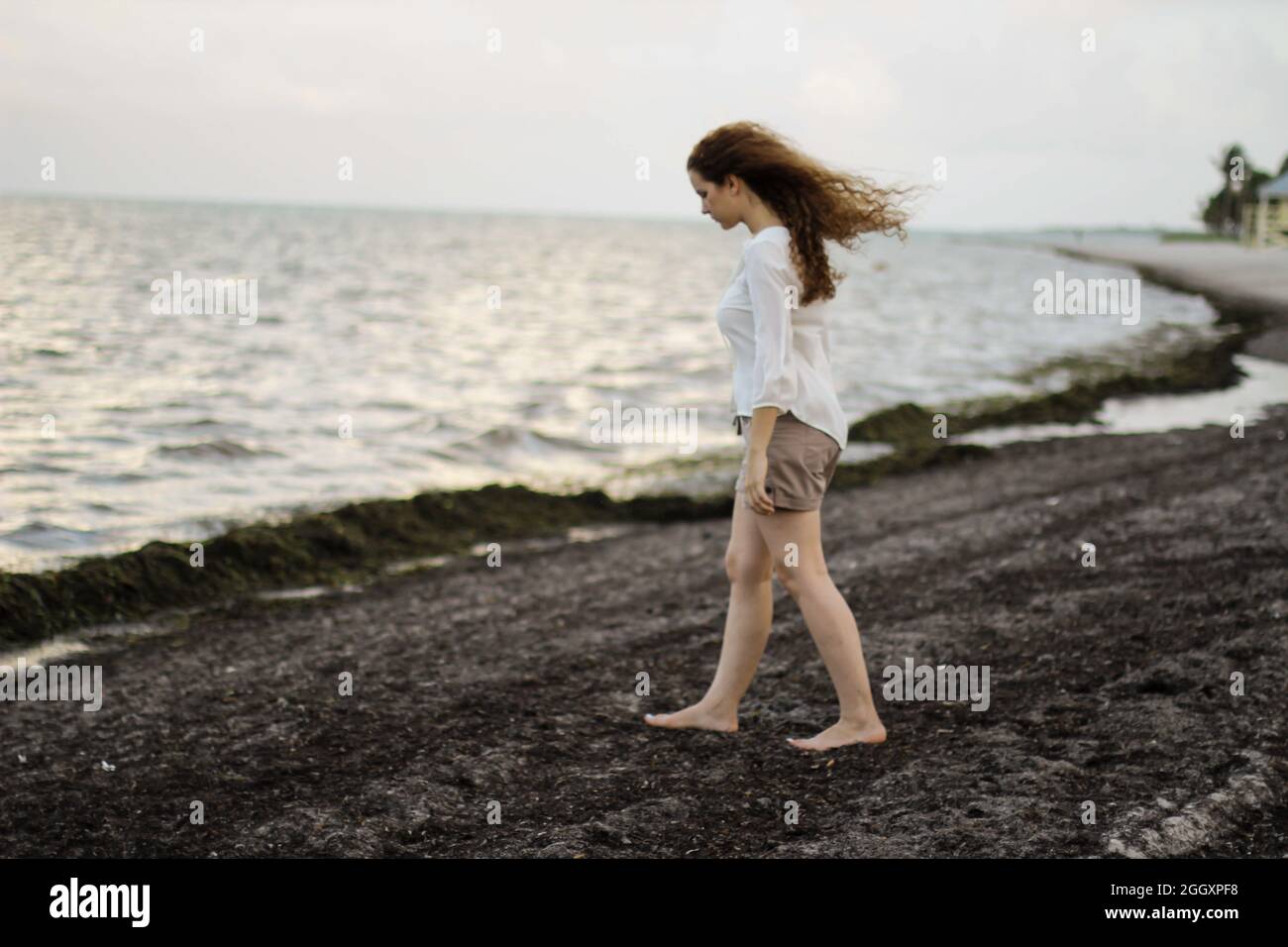 Pensive redhead Caucasian woman walking alone near the shore of the beach Stock Photo