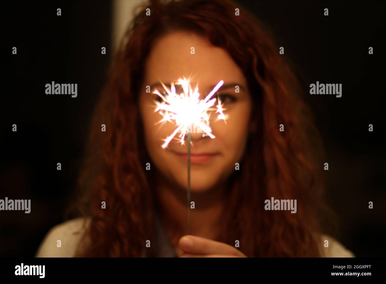 Blurred Young redhead Hispanic and Caucasian holding a sparkler in focus standing in the dark outside Stock Photo