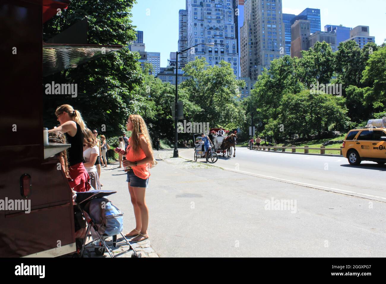 People standing in line outside of Central Park waiting to buy snacks and water. A horse carriage is passing by with people riding it. Stock Photo