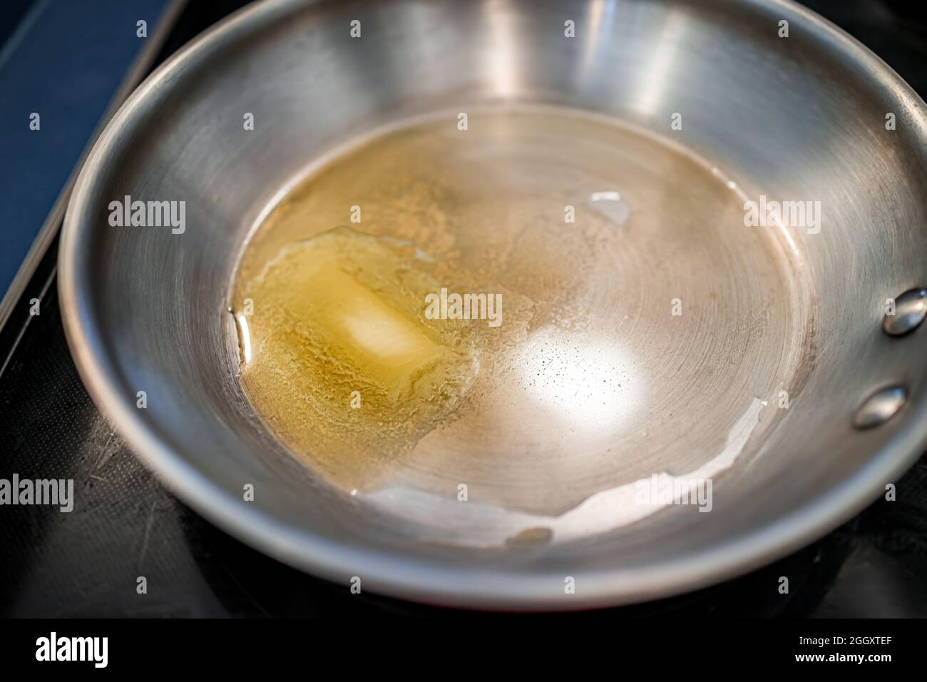 Grassfed butter melting in stainless steel frying pan at high heat