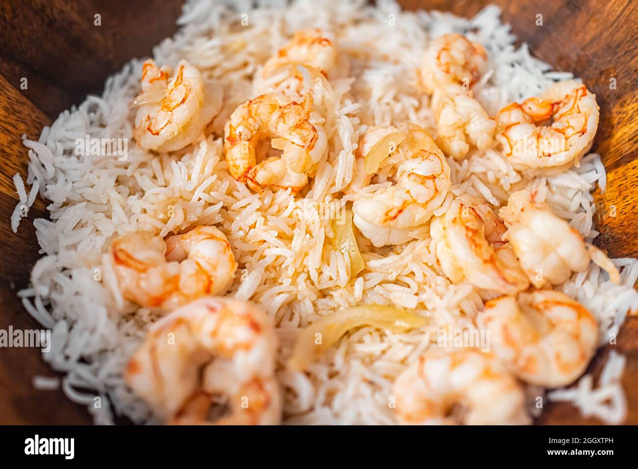 Macro closeup of homemade basmati rice, cooked whole large king jumbo Argentinian fried shrimp seafood with sweet onion slices on wooden plate Stock Photo