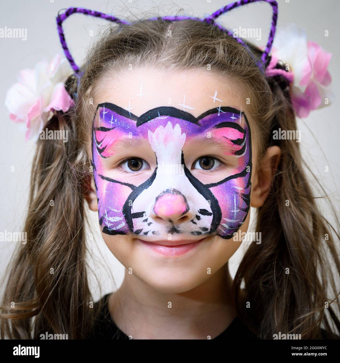 Kid with face painting of kitty, cute little girl with painted mask on her face of rainbow cat. Portrait of pretty child with beautiful makeup, unique Stock Photo