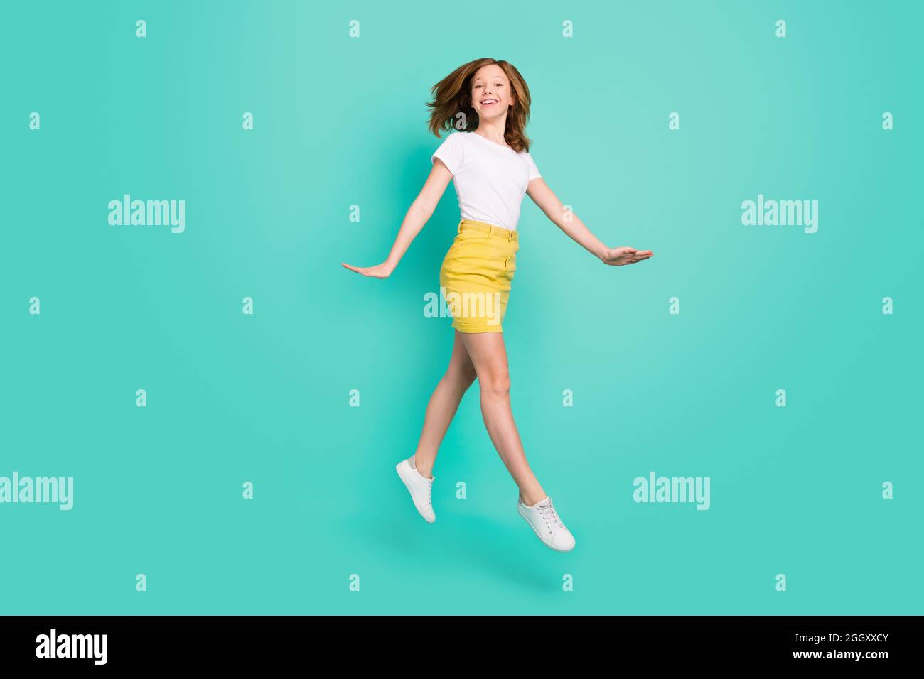 Full length body size photo smiling schoolgirl jumping up careless isolated vivid teal color background Stock Photo