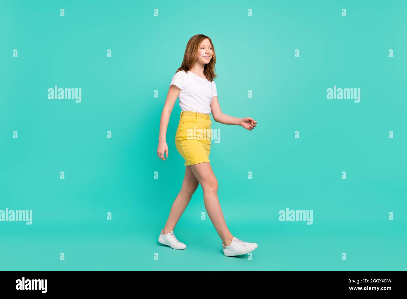 Full length body size photo smiling schoolgirl walking forward looking copyspace isolated vivid teal color background Stock Photo