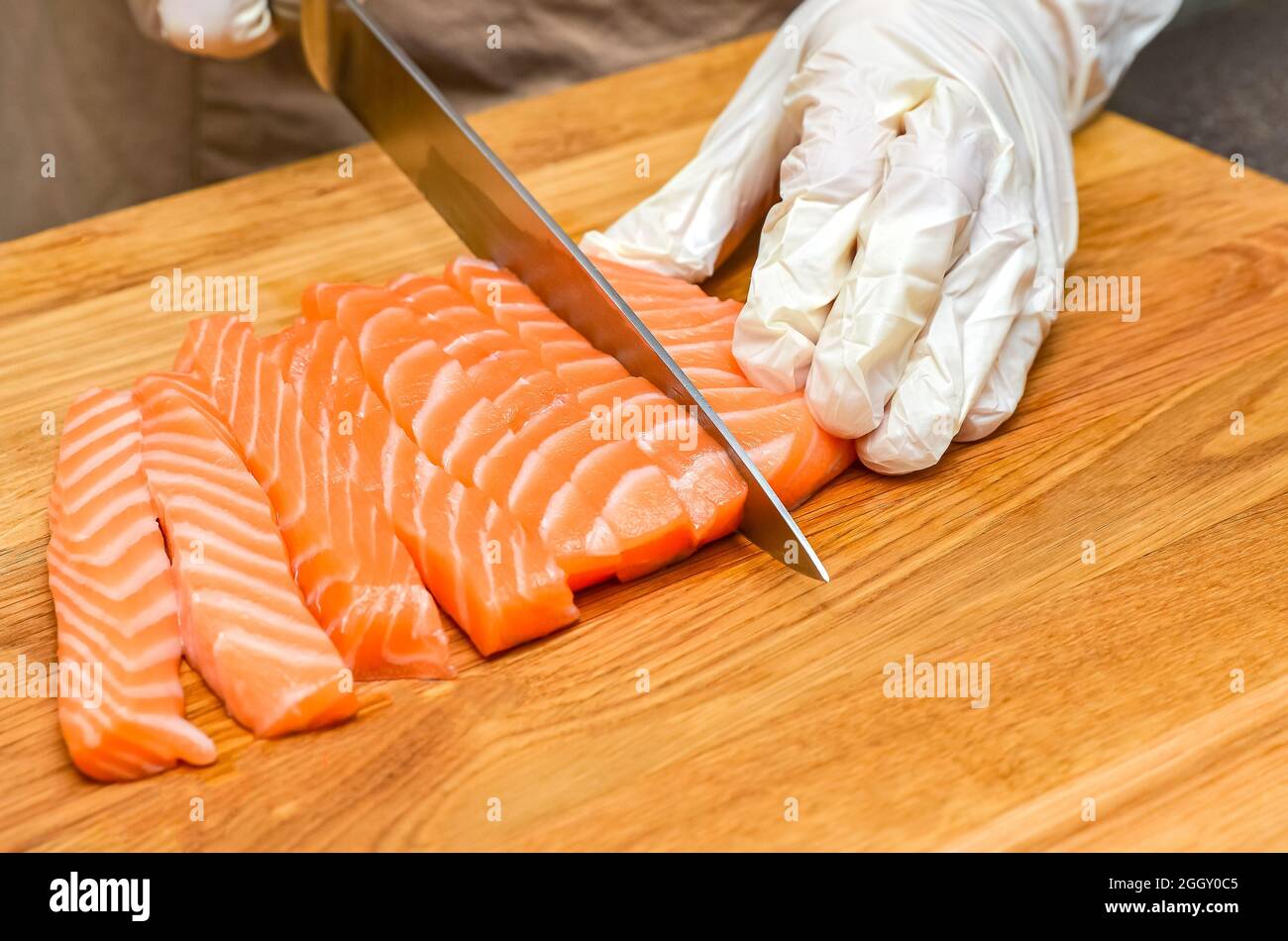 Chef's hands close up. On a wooden cutting board, the chef cuts a red fish with a knife. Stock Photo
