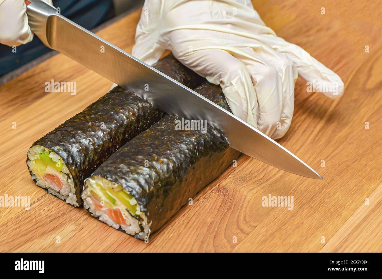 The process of making Japanese sushi. Knife in hand cuts a roll close-up on  a wooden board Stock Photo - Alamy