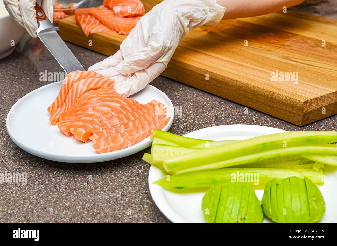 Chef's hands close up. On a wooden cutting board, the chef cuts a red fish with a knife. Stock Photo