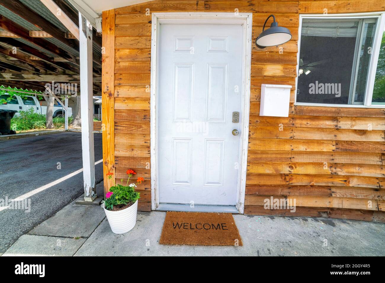 White front door decorated with flowers on a pot and doormat with welcome sign Stock Photo